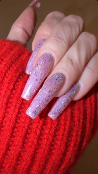 long pink holographic glitter manicure against a red sweater